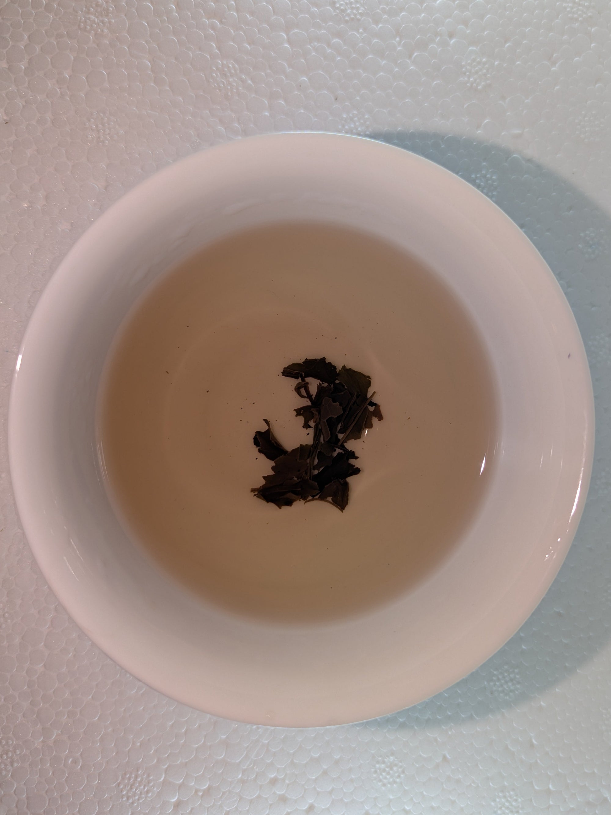 Tea leaves in a small white bowl on a light background