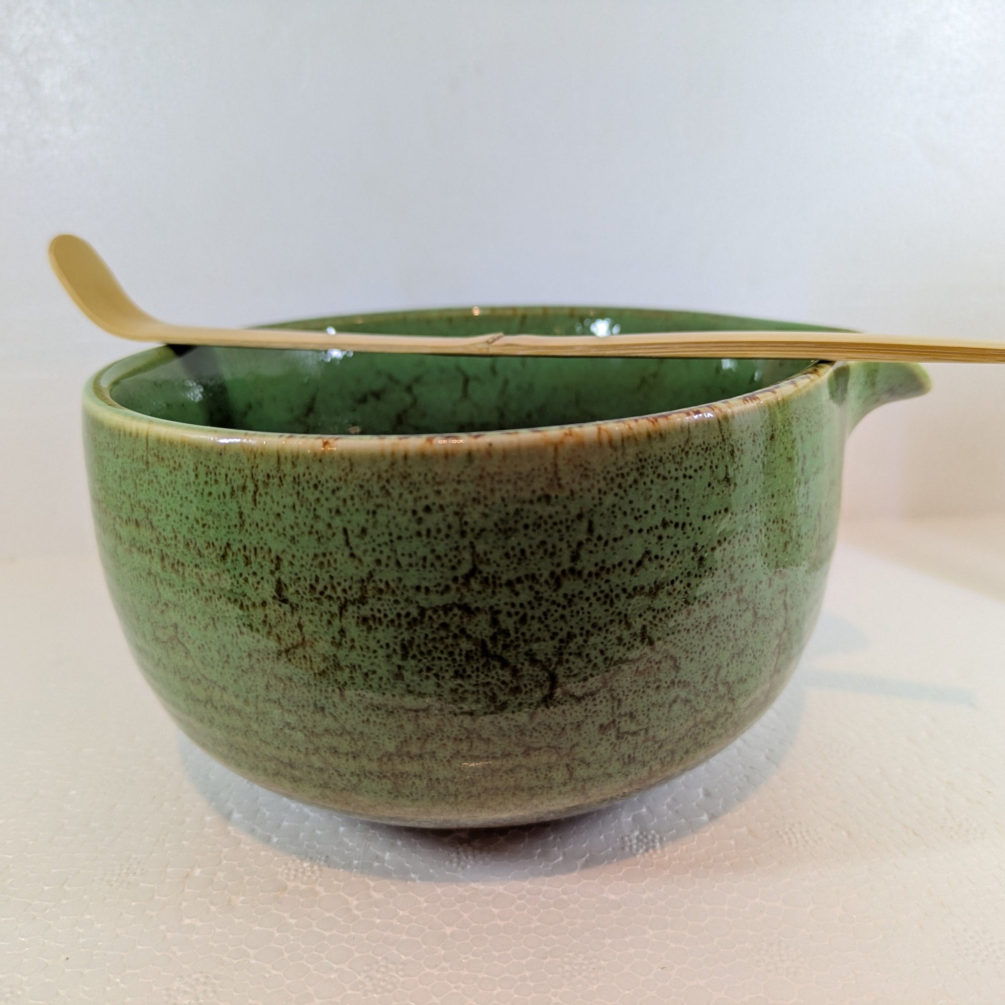 Green ceramic bowl with a wooden spoon on a light background